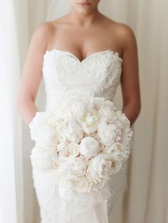 a woman in a wedding dress holding a bridal bouquet with white peonies