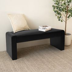 a black bench with a book on it next to a potted plant and a white wall