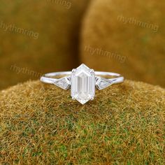 an emerald cut diamond ring on top of moss