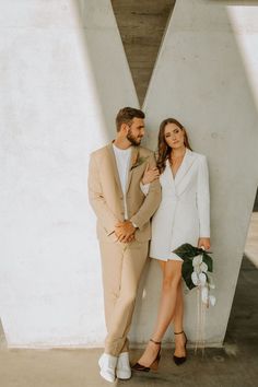 a man and woman standing next to each other in front of a wall with flowers