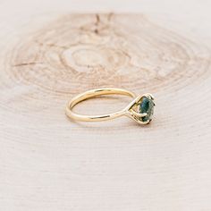 a gold ring with a green stone on it sitting on a wooden surface in front of a piece of wood