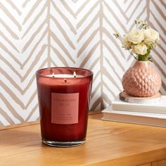 a red candle sitting on top of a wooden table next to a vase with flowers