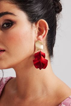 a woman wearing red and gold earrings with flowers on the back of her ear, in front of a white background