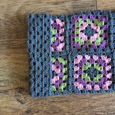 a crocheted square on a wooden floor with the center in purple and green