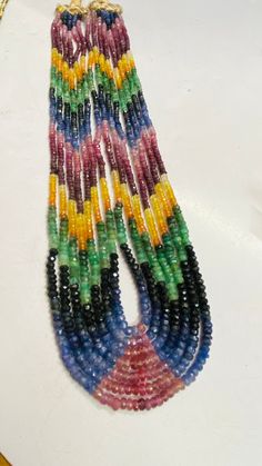 multicolored beads are hanging from a necklace on a white surface with a gold chain