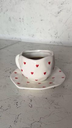 a white cup and saucer with red hearts on it sitting on a gray table