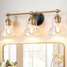 a bathroom vanity with three lights and a mirror on the wall next to flowers in a vase