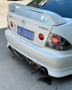 the rear end of a white car parked in front of another car with its license plate on