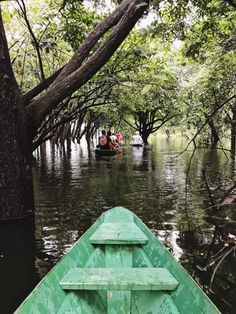 a green boat traveling down a river surrounded by trees and people in the back row