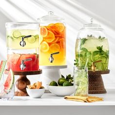 there are many different types of drinks in glass containers on the table with fruit and vegetables