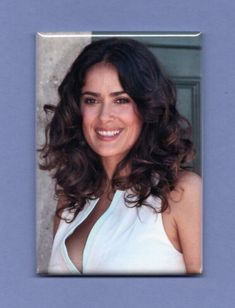 a woman with long dark hair wearing a white top and smiling at the camera while standing in front of a blue wall