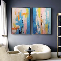 two paintings hang on the wall above a white chair and table in a living room