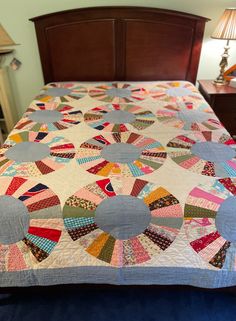 a bed with a large quilt on it's headboard and night stand in the background