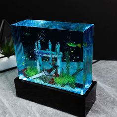 an aquarium with people and fish in it sitting on a table next to a potted plant