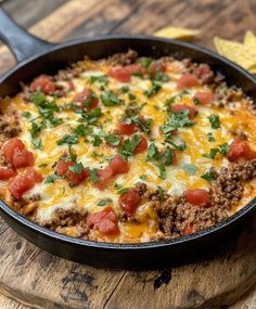 a casserole dish with meat, cheese and tomatoes in a skillet on a wooden board