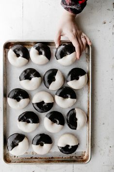 a person reaching for some black and white doughnuts on a baking sheet with one hand