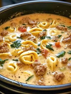 a pot filled with pasta and meatballs in broth, cheese and spinach