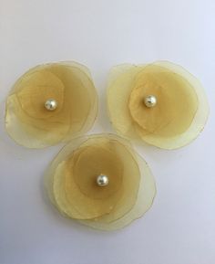 three pieces of yellow paper with pearls in the center on a white tablecloth background