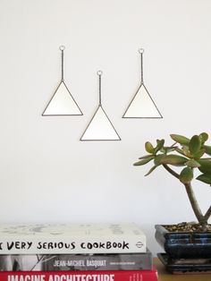 three metal triangles hang from the ceiling above a table with books and a potted plant