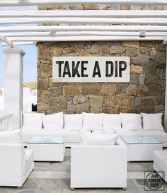 a white couch sitting under a sign on the side of a stone wall next to a chair and ottoman