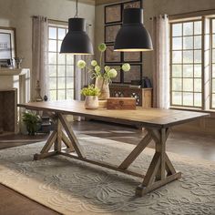 a large wooden table with two lamps on it in front of a fireplace and windows