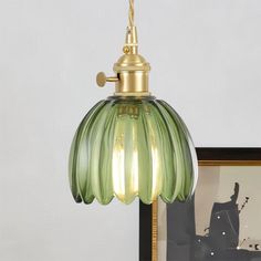 a green glass light hanging from a gold colored ceiling fixture with a black framed photograph in the background