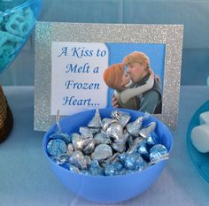 a blue bowl filled with chocolates next to a sign that says, a kiss to melt a frozen heart