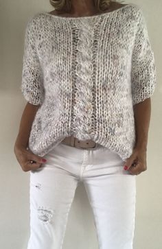 a woman wearing white jeans and a knitted sweater is standing in front of a wall