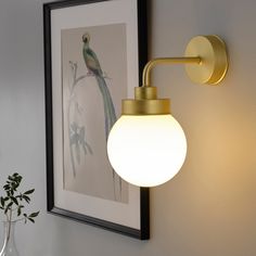 a wall mounted light with a bird on it's side next to a vase