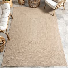 a beige area rug in the middle of a living room with wicker furniture and plants