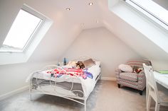 an attic bedroom with a bed, chair and desk in the corner next to two windows