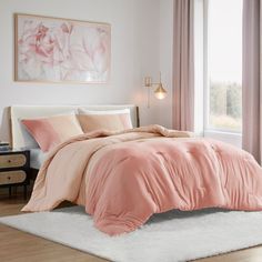 a bed with pink comforter and pillows in a bedroom next to a large window