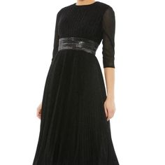 a woman wearing a black dress with sheer sleeves and pleaing on the waist,