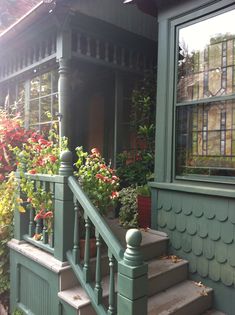 a green house with flowers on the porch and steps leading up to the front door