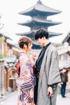 a man and woman standing next to each other in front of a tall pagoda building