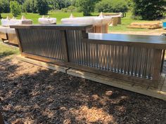 a wooden bench sitting on top of a dirt field next to a forest filled with trees