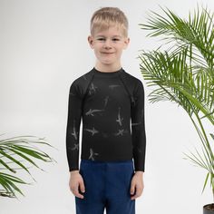 a young boy standing next to a potted plant wearing a black shirt with birds on it