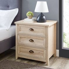 a night stand with two drawers and a lamp on it next to a bed in a bedroom