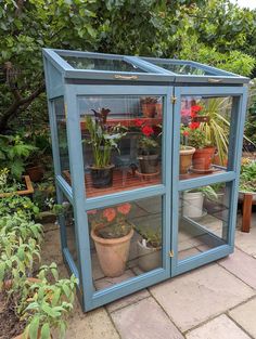 an outdoor greenhouse with potted plants in the front and side glass doors on the inside