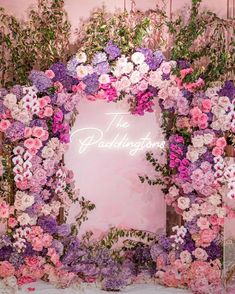 the wedding sign is surrounded by flowers and greenery in front of a pink backdrop