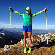 a woman standing on top of a mountain holding two ski poles with both hands in the air