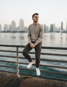 a man is sitting on a rail by the water with his feet in the air