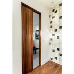 an open door leading to a bathroom with wood flooring and white tiles on the walls