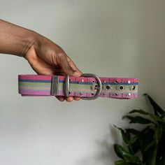 a person is holding onto a pink and green striped belt with silver buckles on it