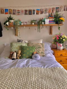 a bed with pillows and stuffed animals on top of it next to a shelf filled with plants