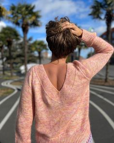 a woman is standing on the street with her back to the camera and looking at palm trees