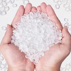 two hands holding small white bubbles in front of a white background with water droplets on it