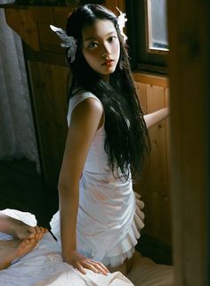 a woman in a white dress sitting on top of a bed next to a window