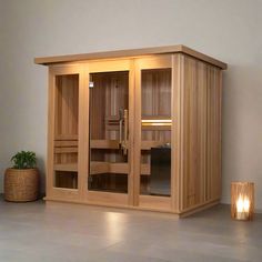 a wooden sauna in a room with candles on the floor and a potted plant next to it