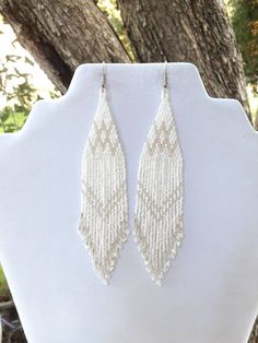 the beaded earrings are hanging from a white mannequin stand in front of a tree